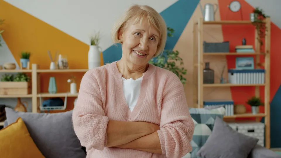 Smiling elderly woman with arms crossed in living room