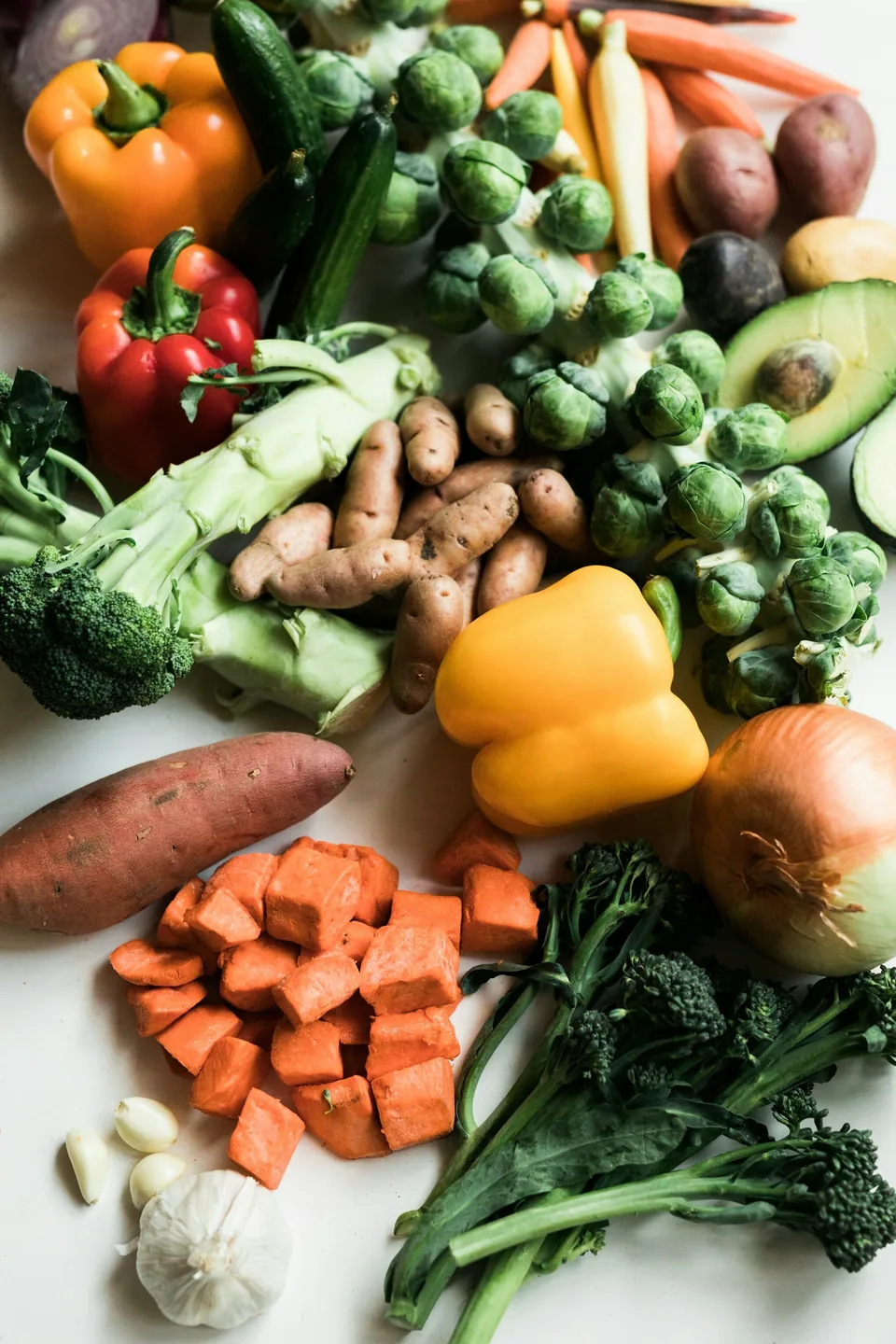 Assorted fresh vegetables including broccoli, peppers, brussels sprouts, and potatoes on a white surface
