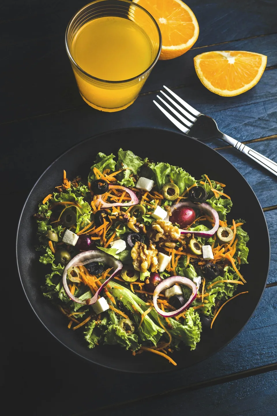 A salad with lettuce, olives, walnuts, and cheese on a dark blue wooden table